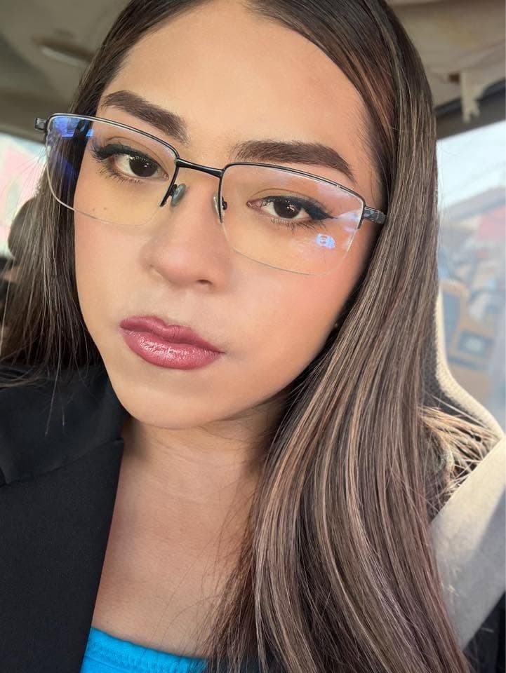 Mujer joven con gafas rectangulares, cabello largo con reflejos y labios de color malva.