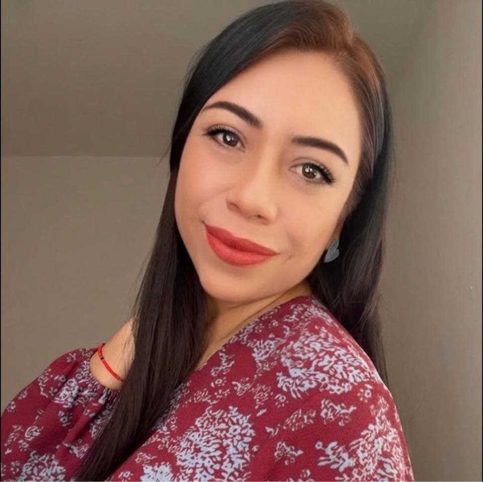 Mujer sonriente con cabello largo oscuro, labios rojos y blusa floral color granate.