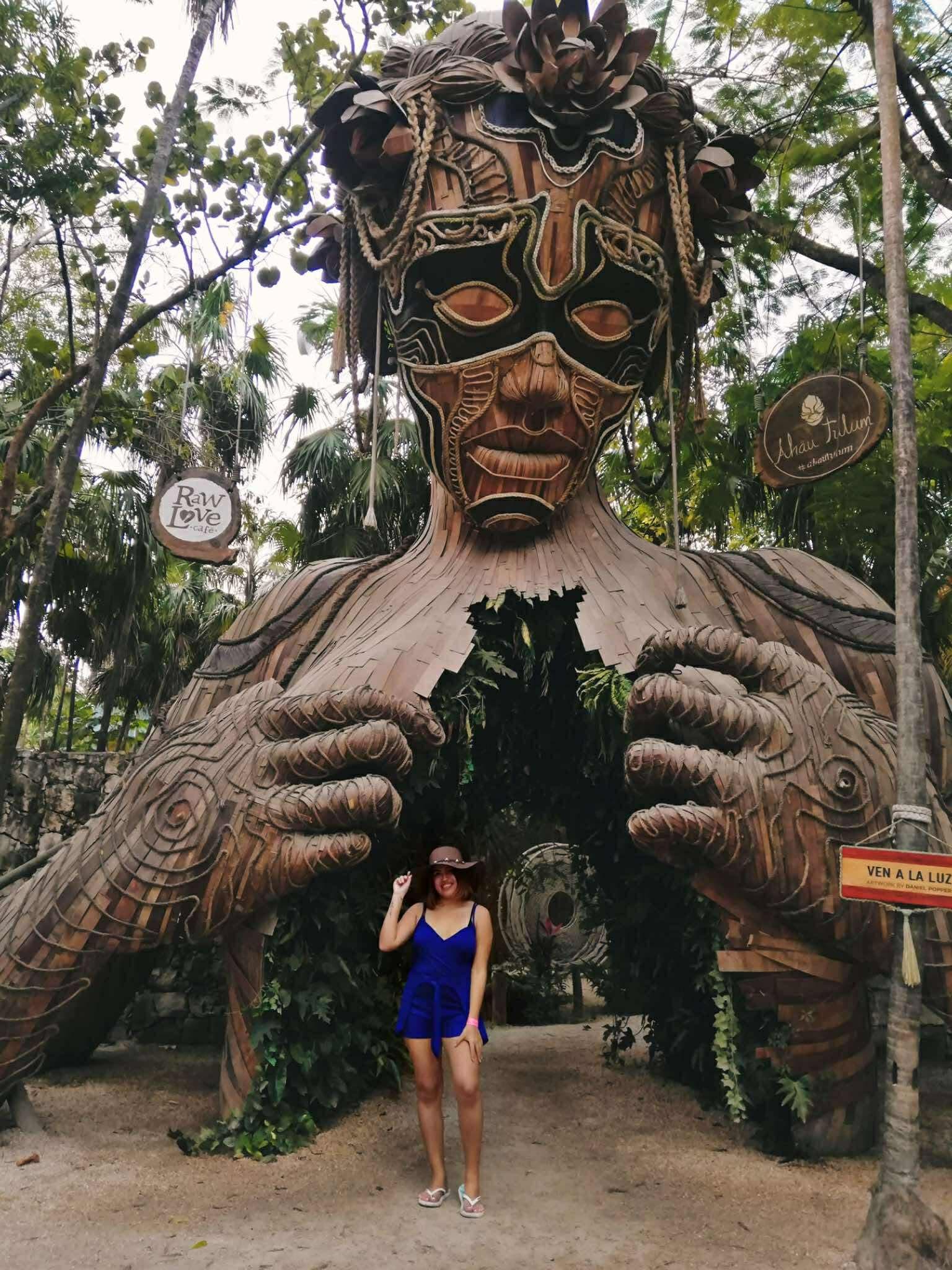 Escultura gigante de madera de una mujer con una persona posando en su pecho abierto.